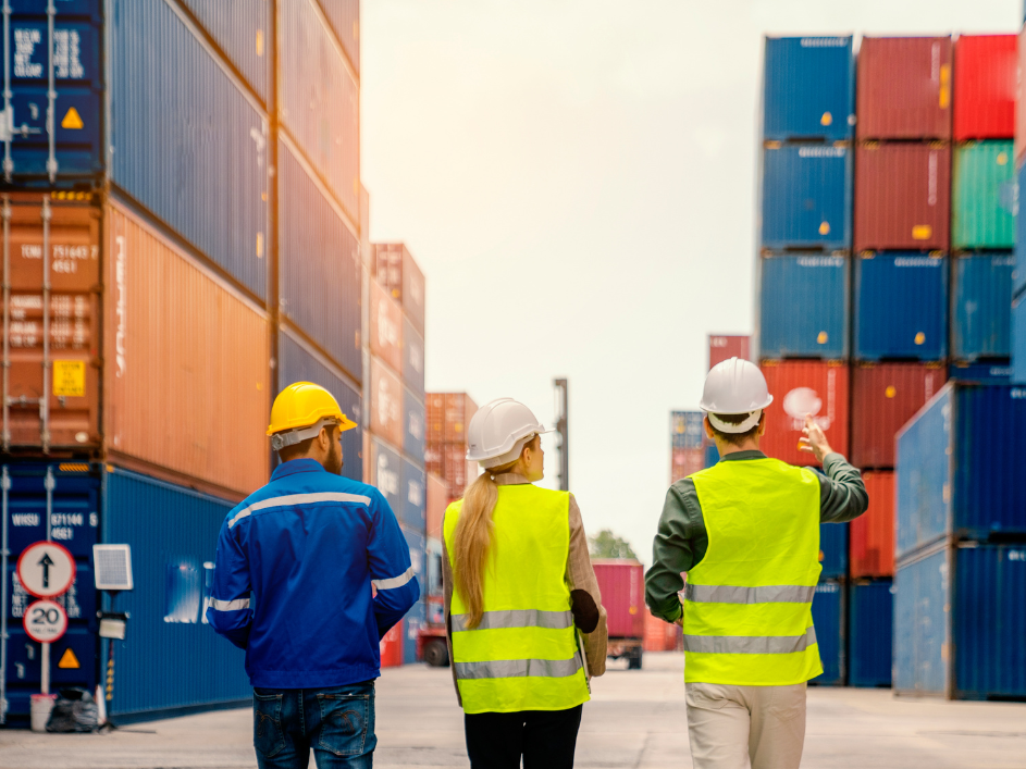 Three researchers in safety gear observing stacks of shipping containers.