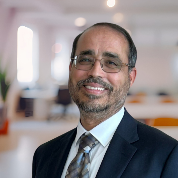 Portrait of Elkafi Hassini, a smiling man wearing glasses and a blue suit and tie.